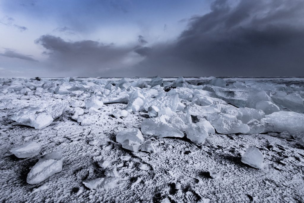 Island. Landschaftsfotografie. Reisefotografie. XL Digitaldruck auf Acryl Alu Dibond. Panoramadruck "icy coast" zeigt mit Schnee bedeckte Eisbrocken auf schwarzem Lavastrand an der Isländischen Küste, dramatische Wolkenformtion. Starke Brandung im Hintergrund. Eisiger Winter. Iceland. XL digital print on acrylic alu dibond. Panoramic image "Icy Coast" shows chunks of glacier ice covered with snow on black lava beach. Coast of Iceland. Dramatic clouds. strong ocean surf in the background. icy winter time. travel photography. landscape phptpgraphy.