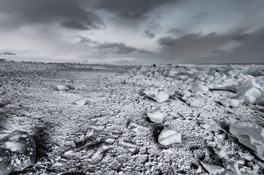 Island. Reisefotografie. Landschaftsfotografie. XL Digitaldruck auf Acryl Alu Dibond. Panoramadruck "Diamond Beach" zeigt mit Schnee bedeckte Eisbrocken auf schwarzem Lavasand an der Isländischen Küste, dramatische Wolkenformtion. Iceland. XL digital print on acrylic alu dibond. Panoramic image "Diamond Beach" shows chunks of glacier ice covered with snow on black lavasand at the beach. Coast of Iceland. Dramatic clouds. winter time. travel photography. landscape phptpgraphy.