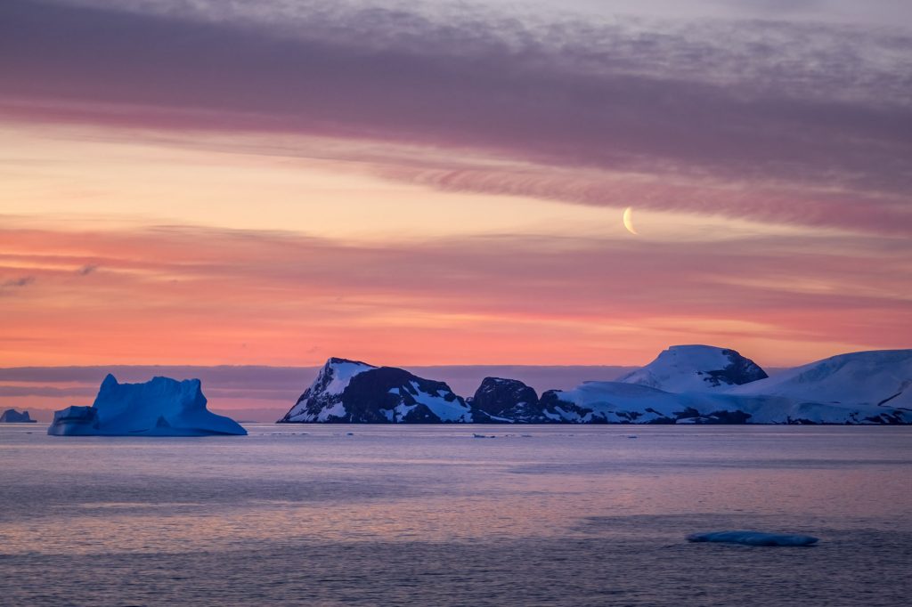 Antarktis. Reisefotografie. Landschaftsfotografie. Digitaldruck auf Acryl Alu Dibond. Fotodruck "Sunset in the Weddell Sea" zeigt Eisbergen und schneebedeckte Berge im antarktischem Meer. Sonnenuntergang mit Mondsichel. Antarctica. XL digital print on acrylic alu dibond. Image "Sunset in the Weddell Sea" shows icebergs and snow covered landscape in the Antarctic Sea after sunset. clouds and cresent moon. Travel Photography. Landscape photography.